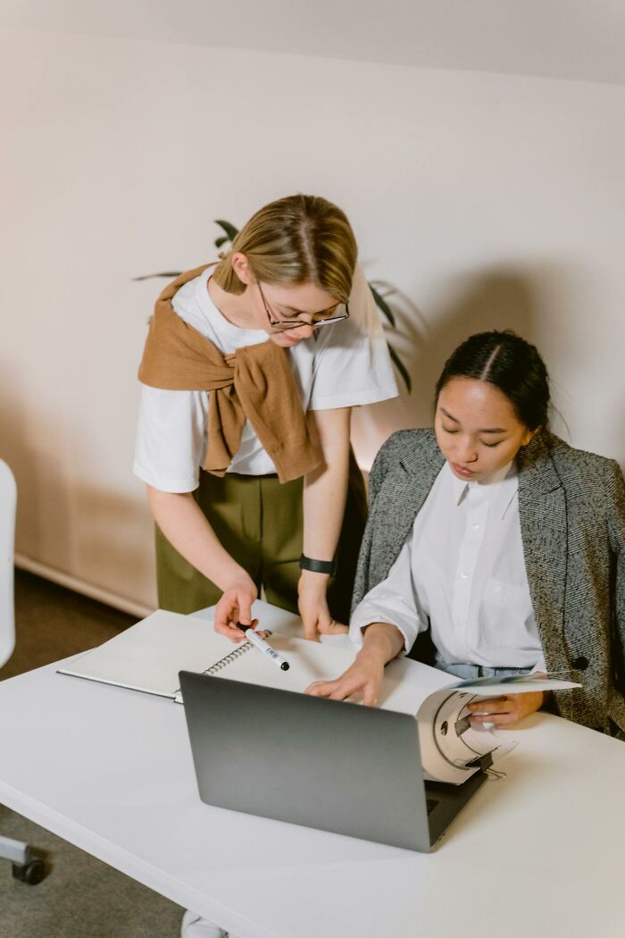 Two women collaborating at a desk with laptop and documents, focused on improving quality of life through teamwork.