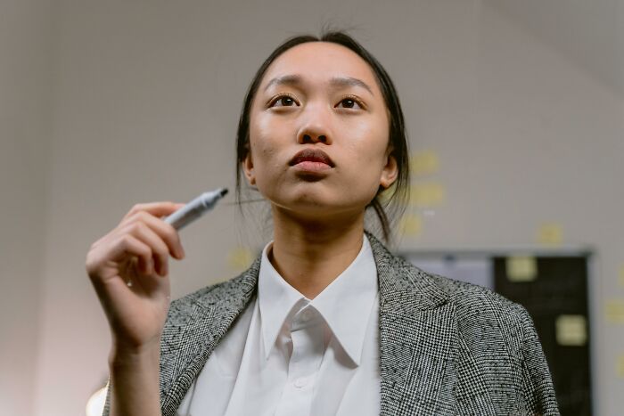 Young woman in a blazer holding a marker, thinking deeply while solving a challenging geography quiz question. Young woman in a blazer holding a marker, thinking deeply while solving a challenging geography quiz question.