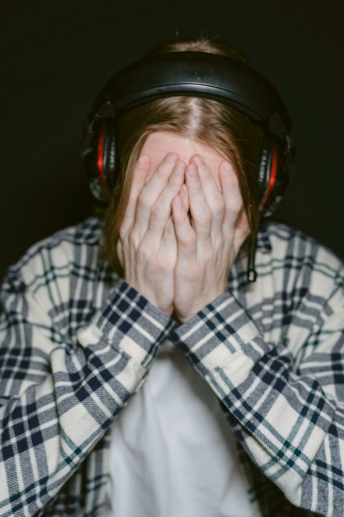 Young person wearing headphones and plaid shirt, covering face in frustration, reflecting middle class challenges.