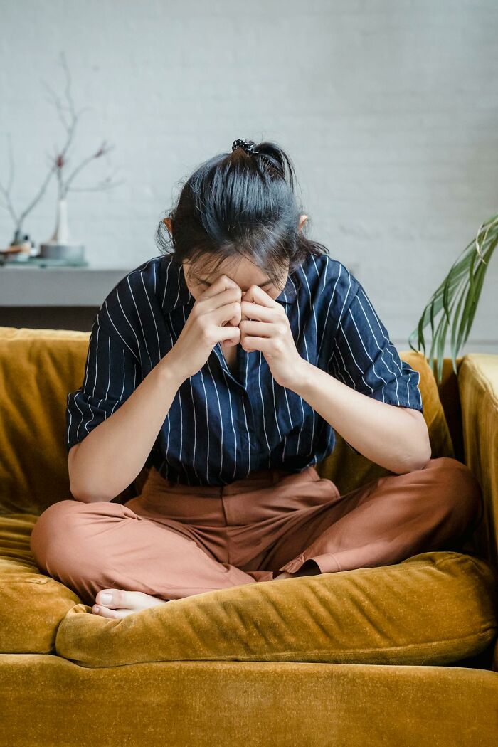 Young woman sitting on a couch with head in hands, showing stress and anxiety about middle class and financial struggles.