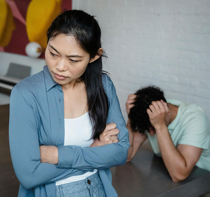 Frustrated ex fiance standing with arms crossed while Valentine day argument unfolds in apartment.