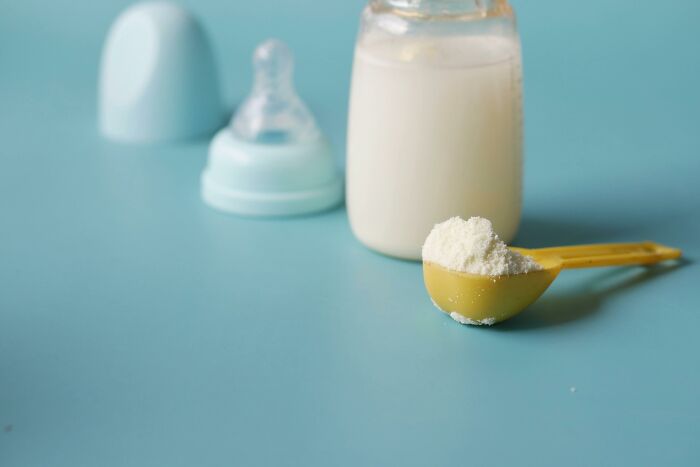 Baby formula powder in a yellow scoop next to a milk bottle on a blue surface highlighting foods that go bad quickly.