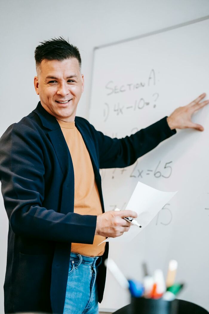 Teacher in a classroom explaining math on a whiteboard, demonstrating things teachers say or do that are unhinged but work