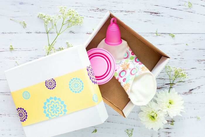 Open gift box with reusable pink menstrual cup and cloth pad, highlighting appalling facts people unaware of feminine care.