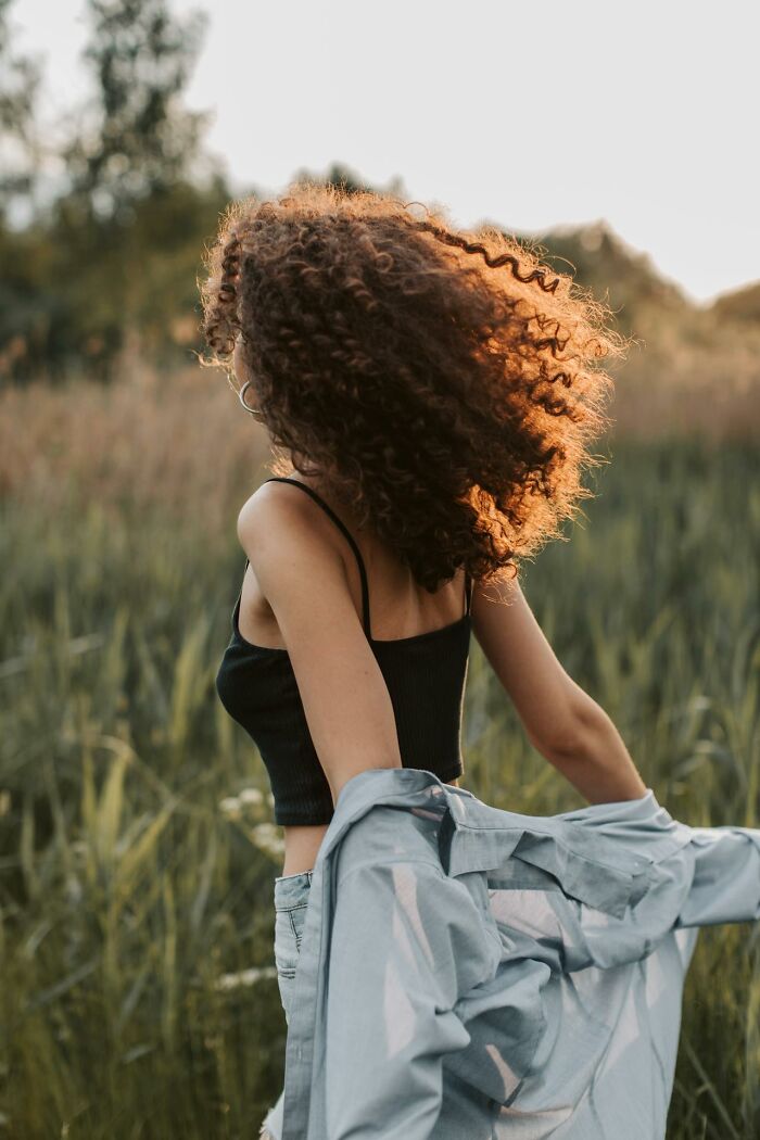 Woman with curly hair outdoors at sunset enjoying nature, representing improved quality of life and happiness.