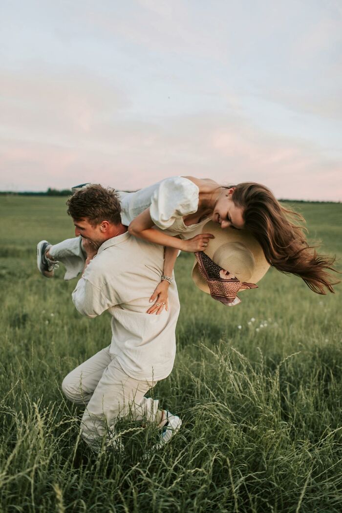 Man lifting woman playfully in a grassy field, contrasting with the theme of women feeling instantly unsafe with a man.