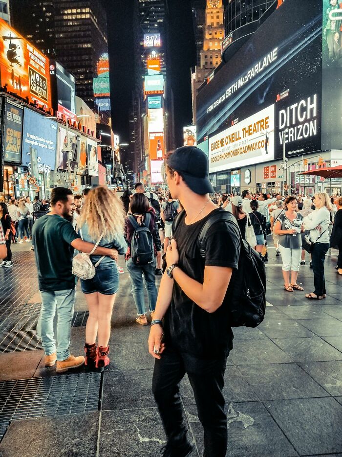 Young man in black clothing stands in crowded city street at night with bright billboards, illustrating serotonin syndrome awareness.