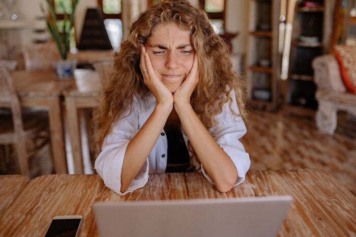 Woman with curly hair looking frustrated while using laptop, illustrating boomer opinions and generational perspectives online.