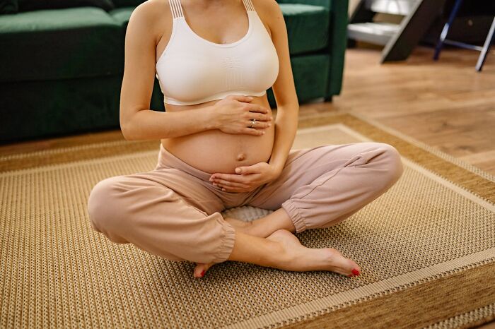 Pregnant woman sitting cross-legged on rug, holding belly with both hands, illustrating serotonin syndrome risks.