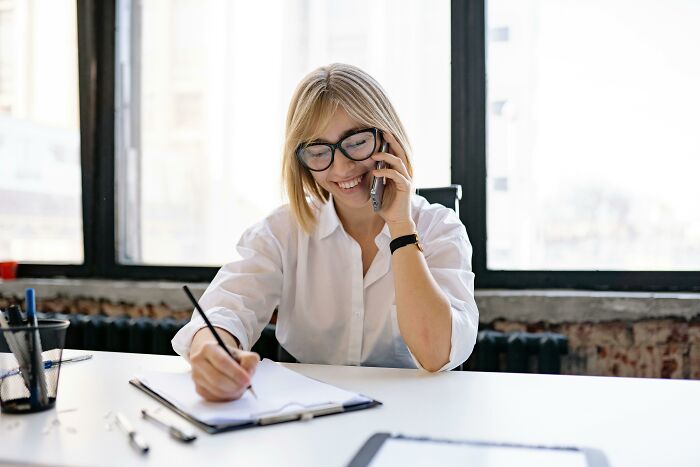 Young woman smiling while talking on the phone and writing notes, illustrating a small decision that changed life forever.