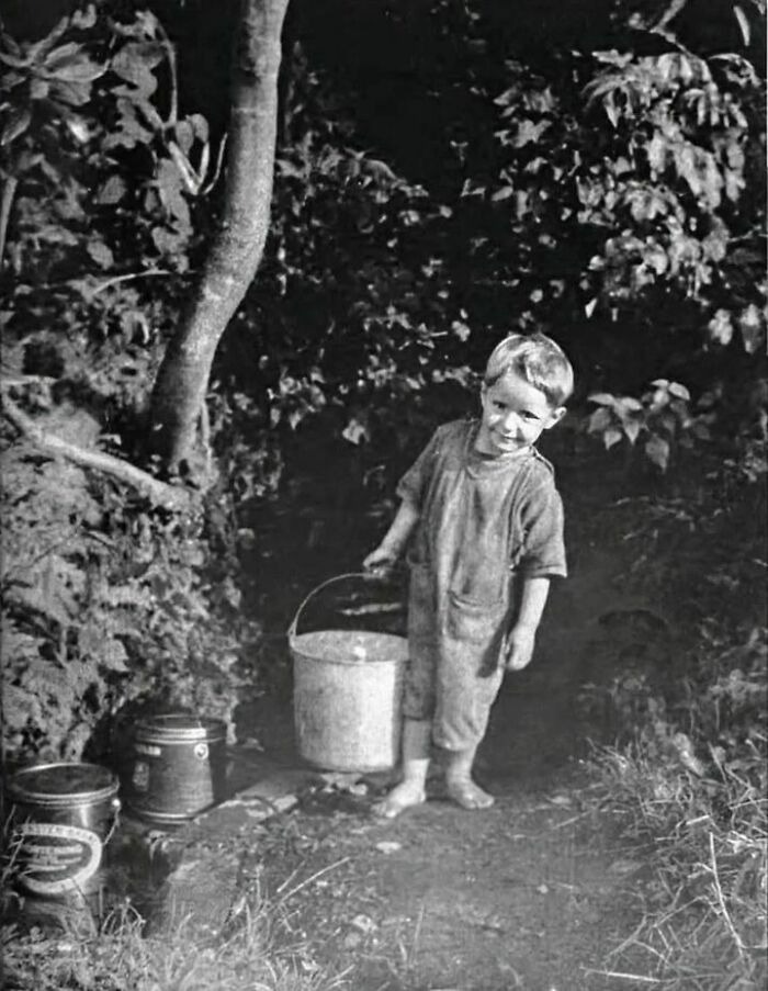 Vintage photo of a barefoot child carrying a metal bucket outdoors, capturing history up close in a natural setting.