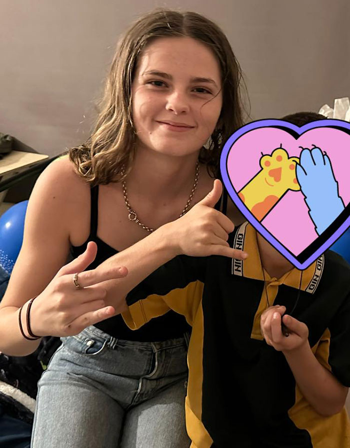 Smiling teenage girl making hand gestures while sitting next to a child with a heart emoji covering their face. Smiling teenage girl making hand gestures while sitting next to a child with a heart emoji covering their face.
