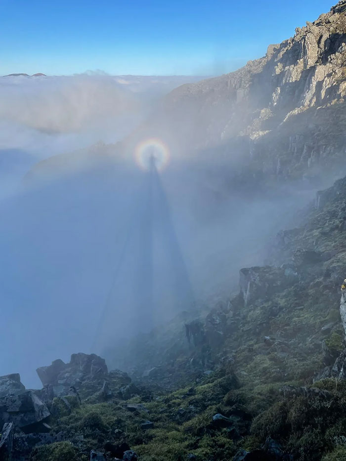 Mountain landscape with fog and a rare natural phenomenon showing a circular rainbow around a shadowed figure.