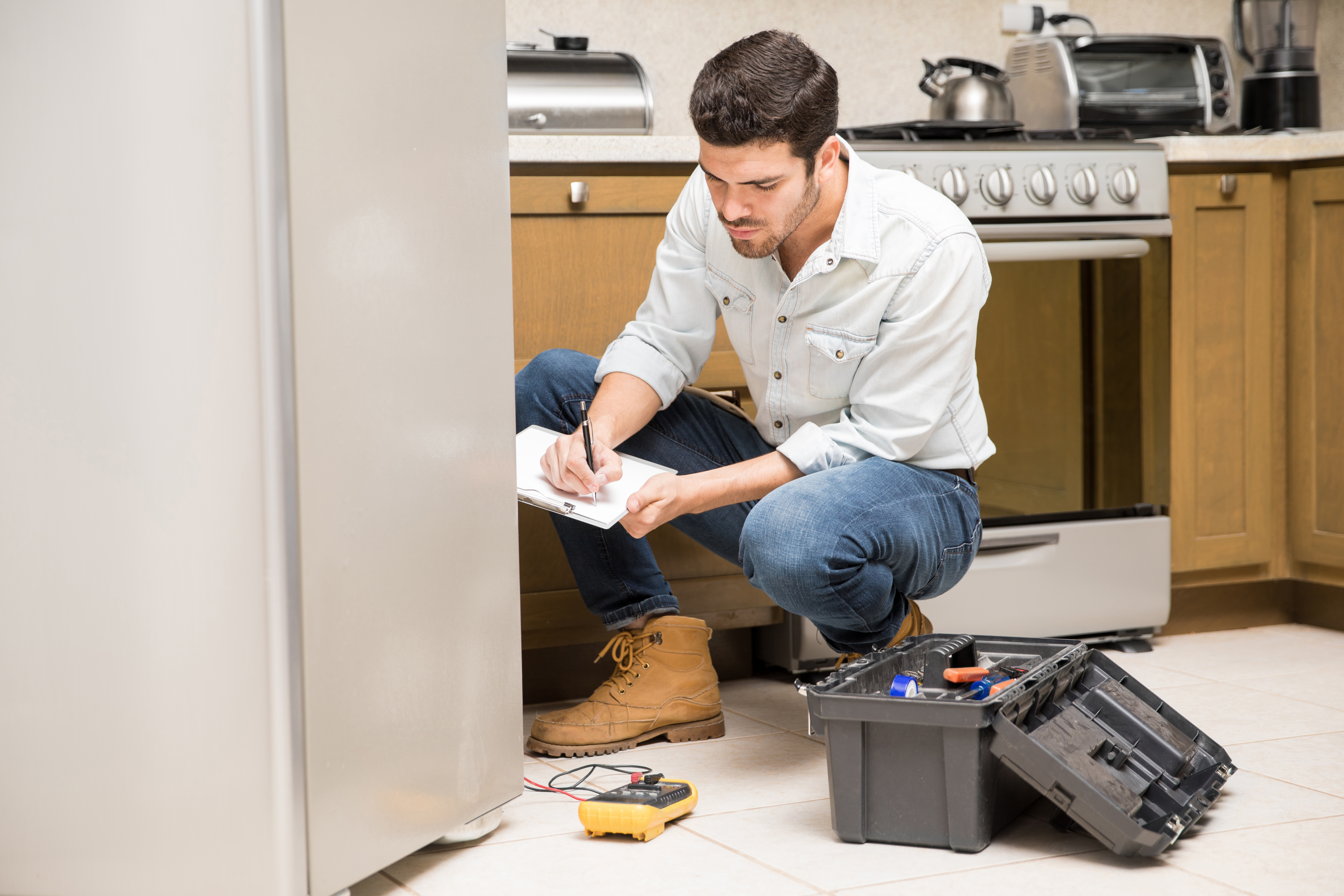 Man in boots and jeans checking refrigerator, taking notes, illustrating husband trying to come clean about a lie.