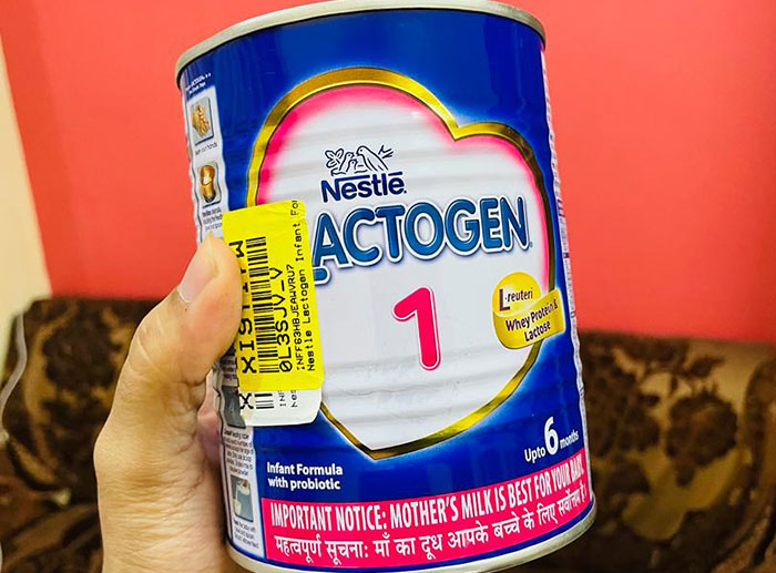 Hand holding a Nestle Actogen infant formula can, highlighting a corporate and PR disaster involving baby formula safety concerns.
