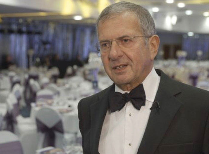 An older man in a tuxedo speaking at a formal event, illustrating a corporate and PR disaster scenario.