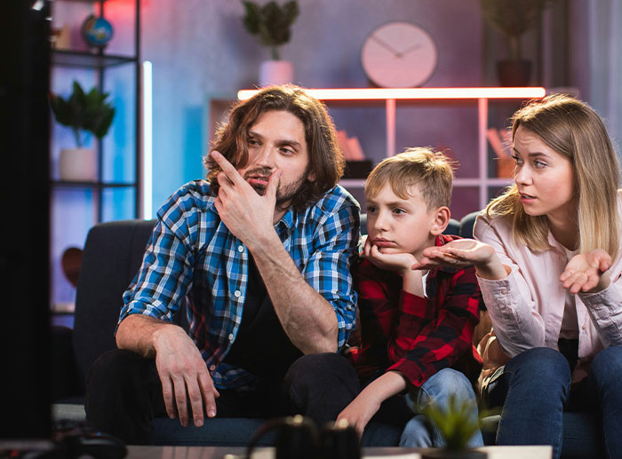 Family sitting on a couch looking frustrated and confused while watching TV, illustrating corporate and PR disasters impact.