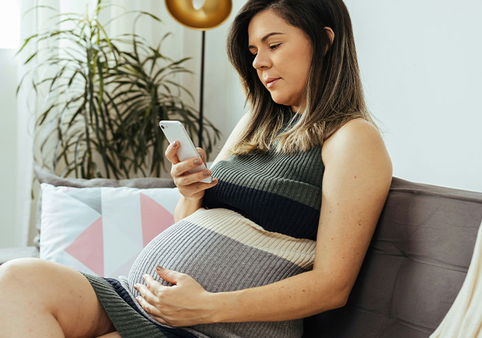 Pregnant woman sitting on couch, holding phone, looking concerned, reflecting emotional impact of gaslighting in marriage.