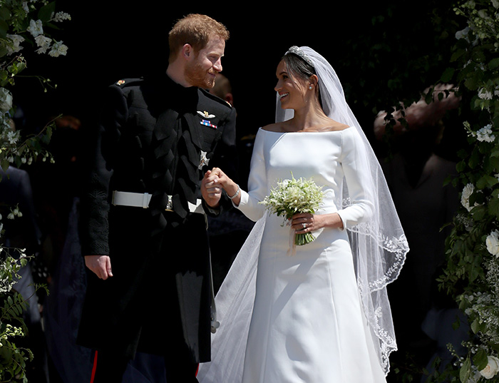 Prince Harry and Meghan Markle holding hands at their wedding, surrounded by floral decorations and guests.