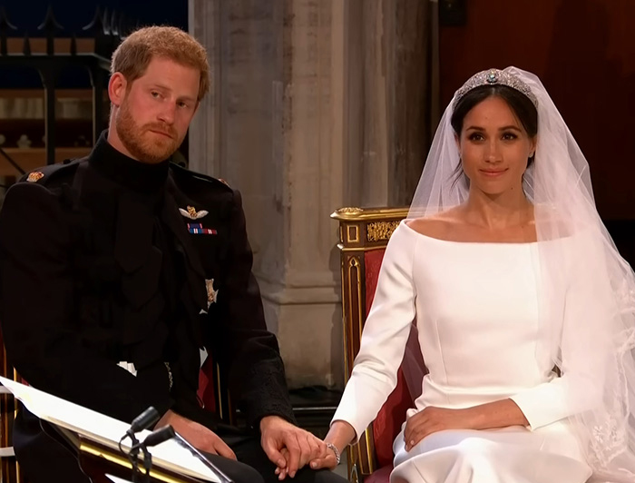 Prince Harry and Meghan Markle holding hands during their wedding ceremony, with Meghan in a bridal gown and veil.