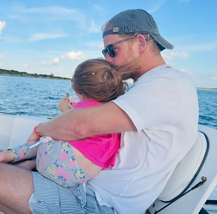 Man wearing sunglasses and cap hugging a toddler on a boat with ocean view, related to Meghan Markle beekeeping clip. Man wearing sunglasses and cap hugging a toddler on a boat with ocean view, related to Meghan Markle beekeeping clip.