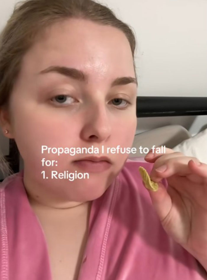 Woman in a pink robe holding a snack, sharing propaganda she refuses to fall for, highlighting religion as the first example.