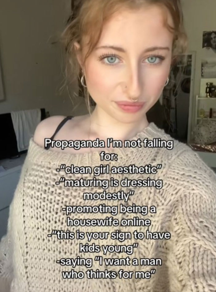 Young woman with blue eyes and nose piercing shares propaganda she refuses to fall for in cozy knit sweater indoors.