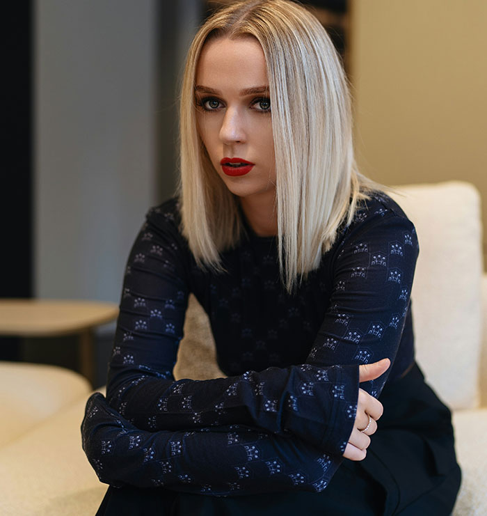 Young woman with blonde hair and red lipstick sitting thoughtfully, reflecting on siblings of narcissists and sociopaths.