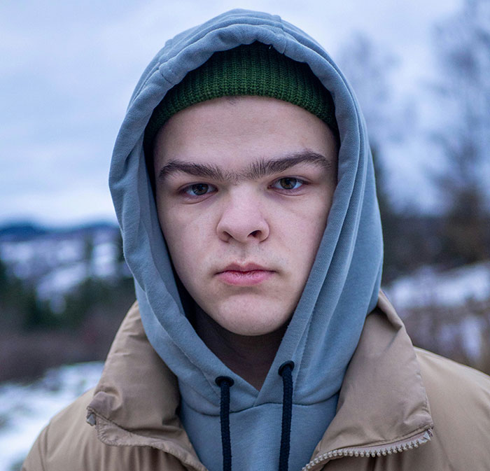 Teenage boy in a hoodie and jacket outdoors, representing siblings of narcissists and sociopaths in emotional distress.