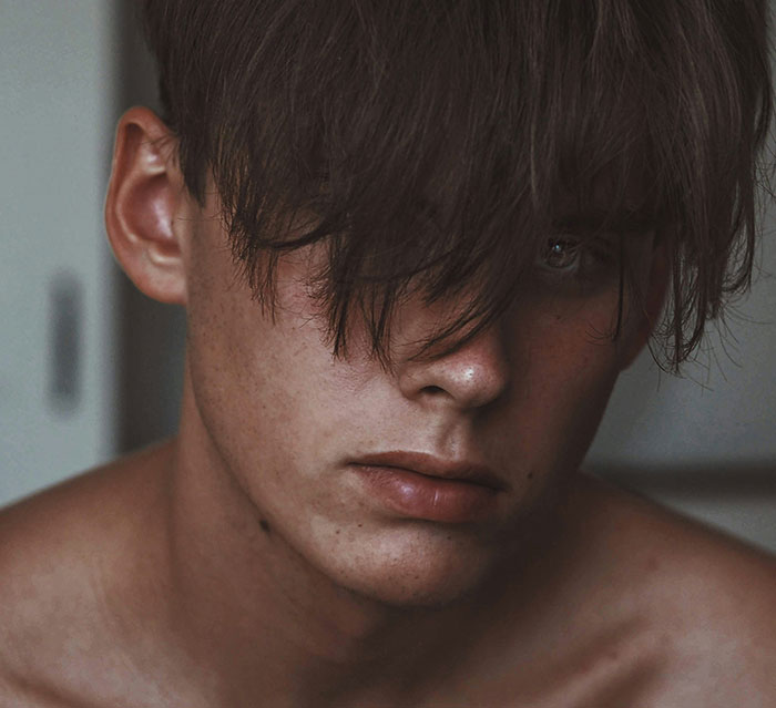 Young man with somber expression partially hidden by hair, symbolizing siblings of narcissists and sociopaths struggles.