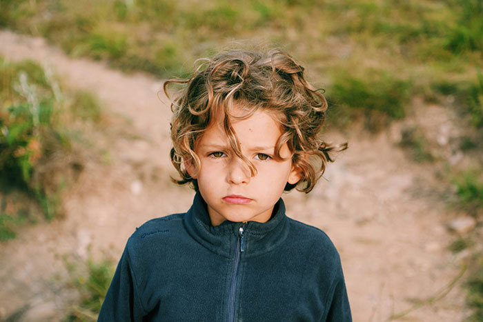 Young child with curly hair looking serious outdoors, representing siblings of narcissists and sociopaths emotions.