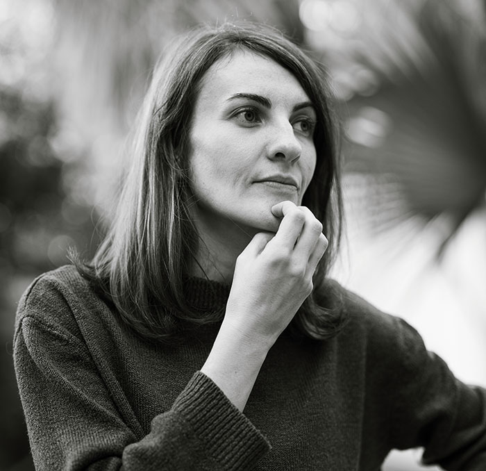 Thoughtful woman with hand on chin, reflecting on complex feelings as sibling of narcissists and sociopaths.