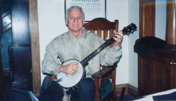 Man sitting on wooden chair playing banjo indoors in a casual setting, related to celebrity encounters gone well or bad.