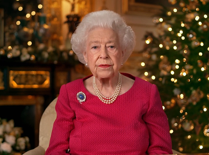 Queen Elizabeth in a formal setting, wearing a red dress and pearl necklace, related to Meghan Markle wedding caterer incident.