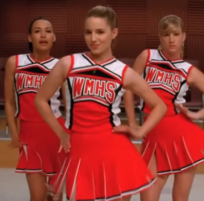Former Glee star Dianna Agron in red WMHS cheerleading outfit performing a dance routine on stage.