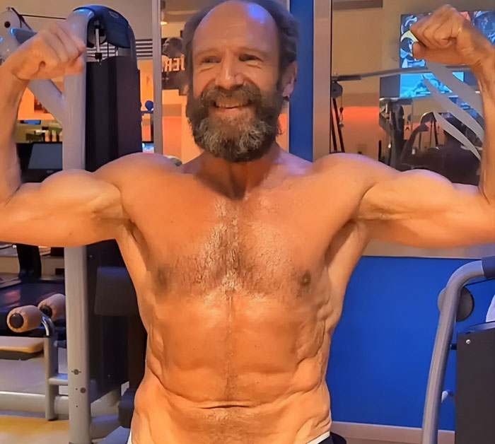 Ralph Fiennes flexing muscles and smiling at gym, highlighting strength and fitness decades after scandalous affair.