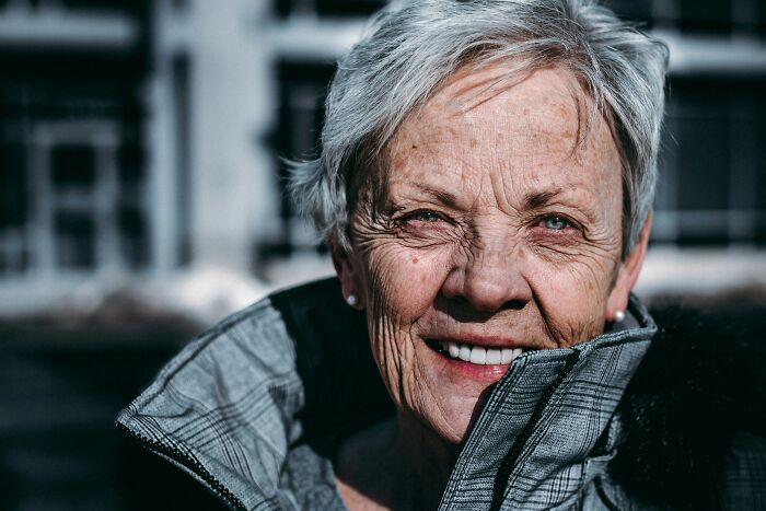 Elderly woman with gray hair and wrinkles smiling outdoors, showing common body changes of aging and getting older.