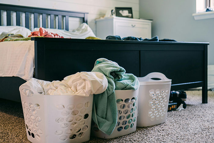 Three laundry baskets filled with clothes in a bedroom with a black bed frame and carpeted floor, illustrating amusing moments.