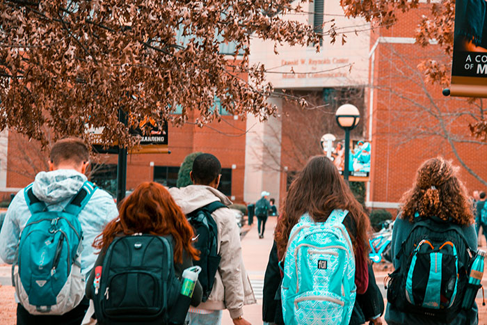 Group of students walking on campus with backpacks, symbolizing people taking huge risks for no logical reason.