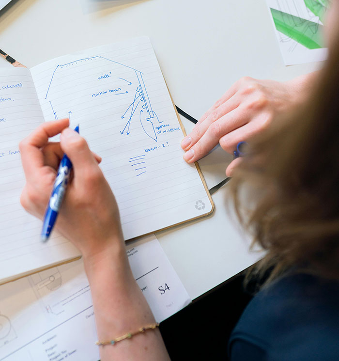 Person sketching and taking notes in a notebook, illustrating concepts about wind made by trees and natural beams.