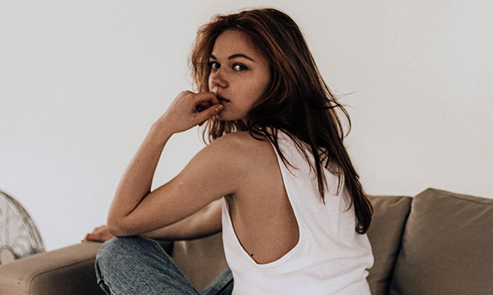 Young woman sitting on a couch, looking thoughtful, illustrating moments people realized their partner wasn’t the brightest.