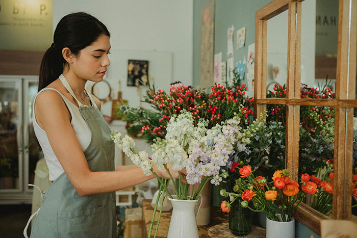 Young woman arranging flowers in a shop, illustrating people taking huge risks for no logical reason in everyday situations.
