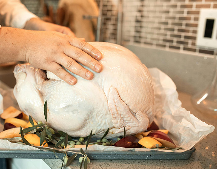 Person preparing raw turkey on baking tray with fruit and herbs, illustrating funny moments about wind made by trees.