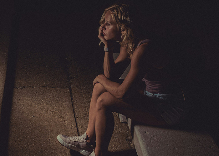 Woman sitting alone in the dark looking thoughtful, representing raw stories of parents disowning their kids.