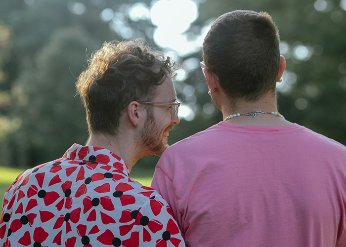 Two young men sitting outdoors, one in a patterned shirt and the other in a pink shirt, representing stories of parents disowning kids.