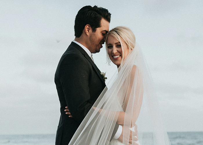 Bride and groom embracing on a beach, highlighting emotional contrasts in stories of parents disowning their kids.