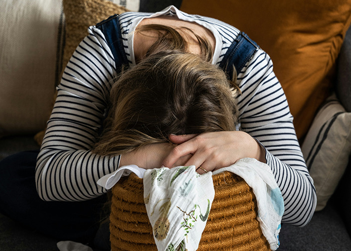 Woman in a striped shirt sitting with head down on a basket, conveying emotion in stories of parents disowning their kids.