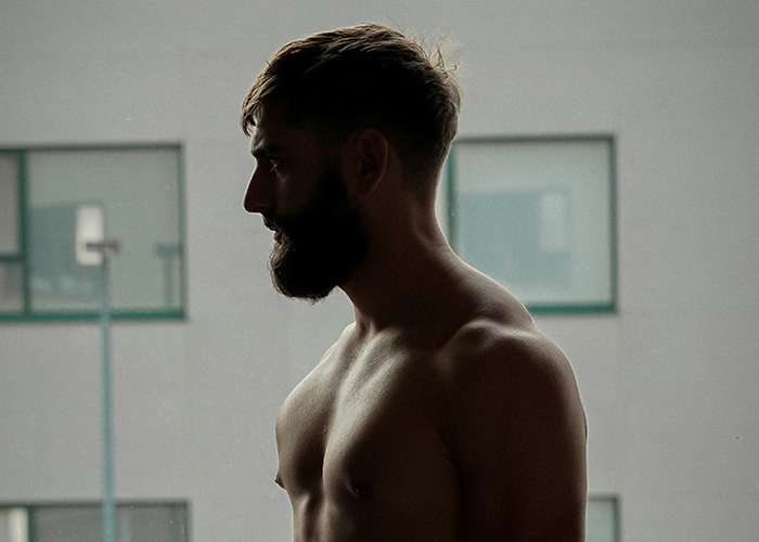 Silhouetted shirtless man with beard standing indoors by a window, reflecting on difficult parenting and disowning stories.