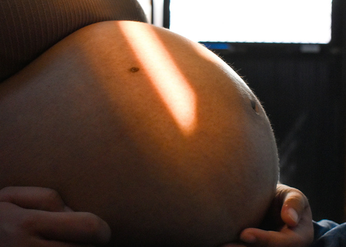 Close-up of a pregnant belly lit by soft sunlight, symbolizing themes of parents and family challenges.