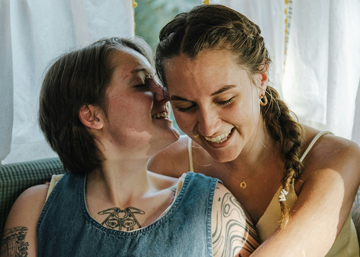 Two young women smiling and sharing a close moment, highlighting complex emotions of parents disowning their kids.